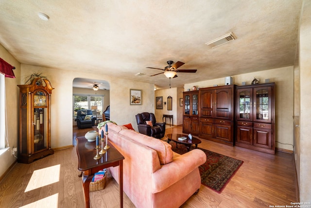 living room featuring a ceiling fan, baseboards, visible vents, arched walkways, and light wood-style floors