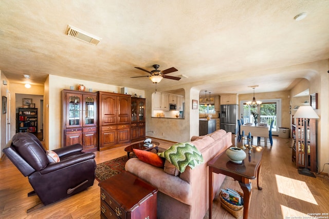 living room featuring arched walkways, visible vents, light wood-style flooring, and ceiling fan with notable chandelier