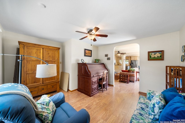 living room featuring arched walkways, light wood-style flooring, baseboards, and a ceiling fan