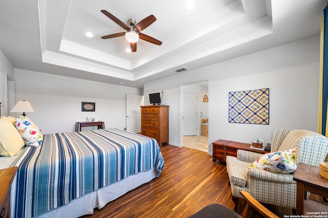 bedroom featuring a raised ceiling, wood finished floors, visible vents, and ornamental molding