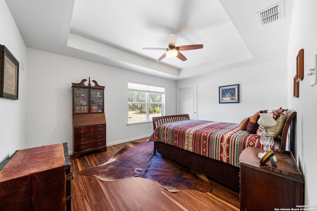 bedroom featuring visible vents, baseboards, wood finished floors, a raised ceiling, and a ceiling fan