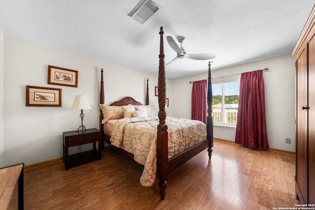 bedroom featuring visible vents, a textured ceiling, baseboards, and wood finished floors