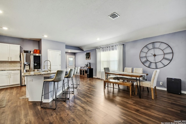 kitchen featuring visible vents, a center island with sink, a kitchen bar, light stone counters, and dark wood-style floors