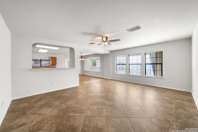 unfurnished living room with visible vents, baseboards, ceiling fan, arched walkways, and tile patterned floors