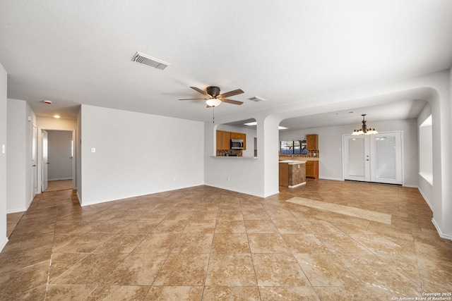 unfurnished living room featuring ceiling fan with notable chandelier, visible vents, and baseboards