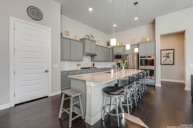 kitchen with light stone countertops, gray cabinets, backsplash, and stainless steel appliances