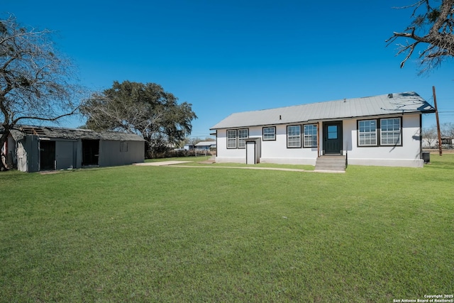 back of house with a lawn, an outdoor structure, metal roof, and stucco siding