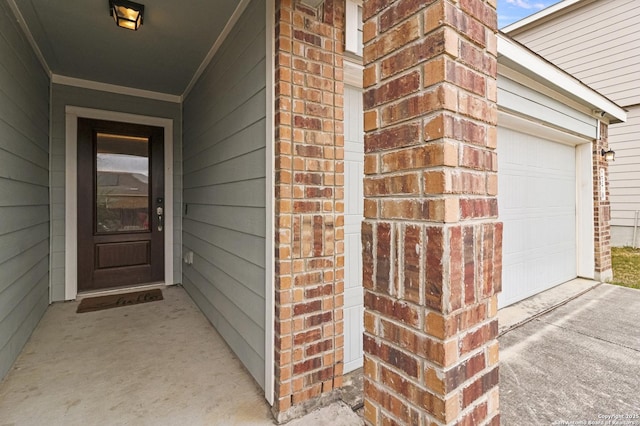 view of exterior entry featuring driveway, brick siding, and an attached garage