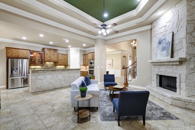 living area with a ceiling fan, arched walkways, a stone fireplace, stairs, and crown molding