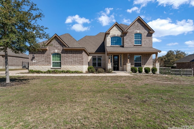 french provincial home with brick siding, stone siding, a front lawn, and fence