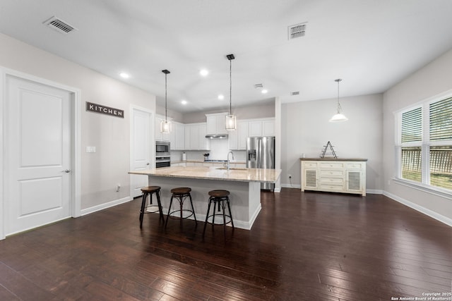 kitchen with dark wood-type flooring, light stone counters, appliances with stainless steel finishes, and a sink