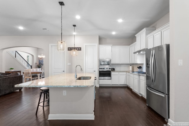 kitchen with arched walkways, a sink, stainless steel appliances, under cabinet range hood, and white cabinetry