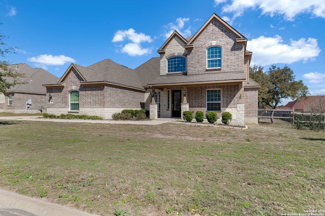 french country style house with brick siding, a shingled roof, a front lawn, and fence