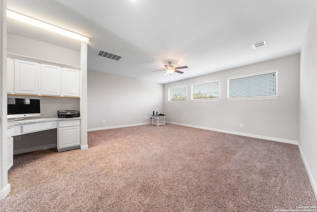 unfurnished living room featuring visible vents, a ceiling fan, baseboards, light colored carpet, and built in study area