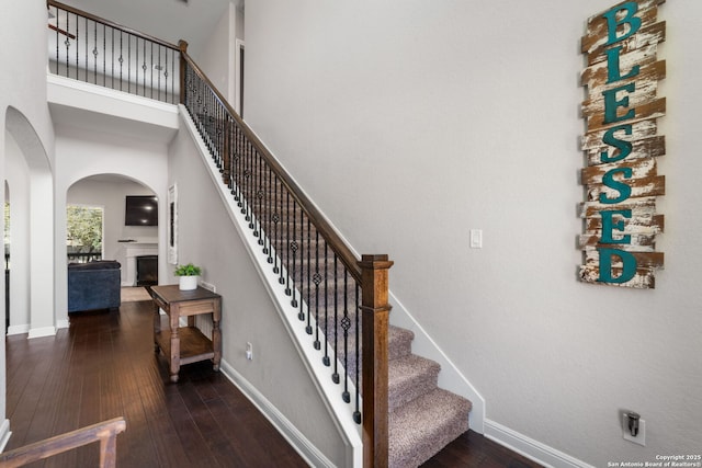 stairs with hardwood / wood-style floors, a fireplace, arched walkways, and baseboards