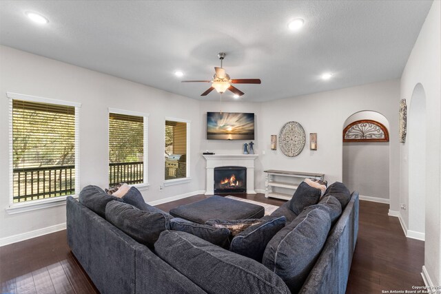 living room featuring dark wood finished floors, baseboards, a lit fireplace, and ceiling fan