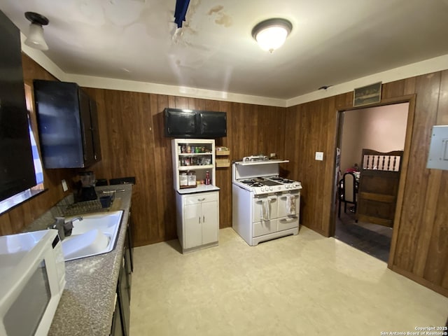 kitchen featuring dark countertops, wood walls, light floors, white appliances, and a sink