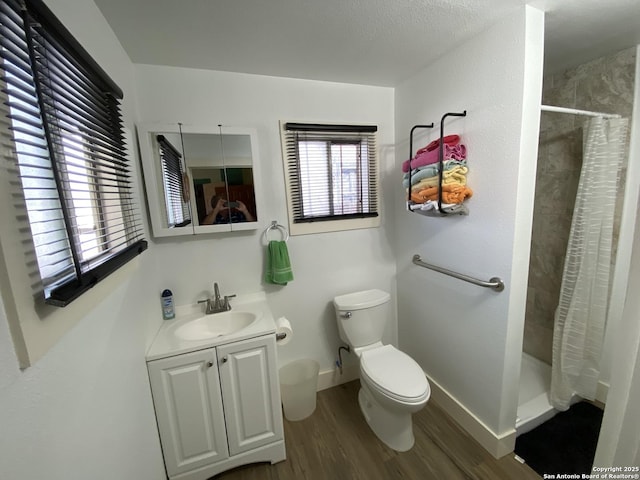 bathroom with toilet, wood finished floors, a shower stall, baseboards, and vanity