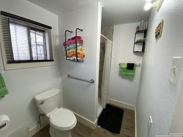 bathroom featuring toilet, a shower with shower curtain, baseboards, and wood finished floors