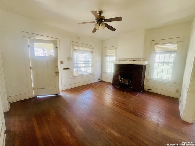 unfurnished living room featuring plenty of natural light, a brick fireplace, ceiling fan, and wood finished floors