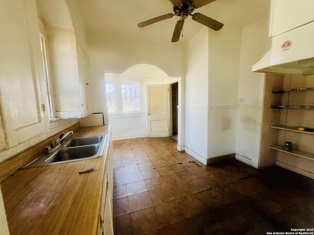 kitchen with baseboards, wooden counters, a high ceiling, a sink, and ceiling fan