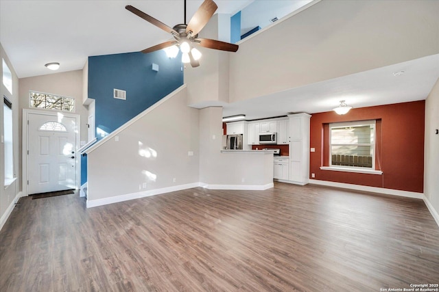 unfurnished living room with visible vents, high vaulted ceiling, a ceiling fan, wood finished floors, and baseboards