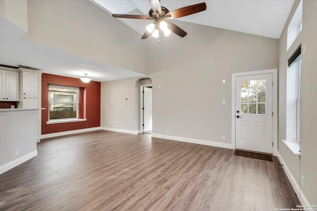 unfurnished living room featuring ceiling fan, baseboards, arched walkways, and wood finished floors