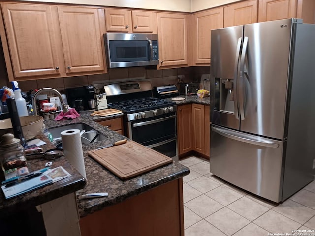 kitchen with a sink, dark stone countertops, appliances with stainless steel finishes, light tile patterned flooring, and decorative backsplash