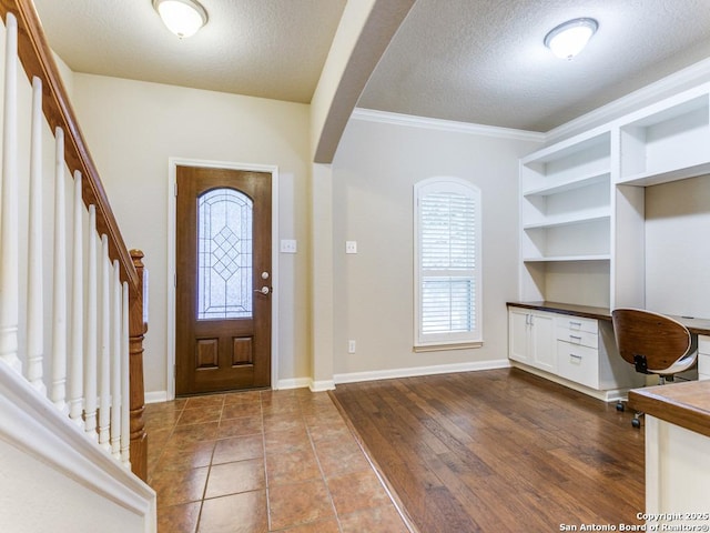 entrance foyer featuring dark wood finished floors, stairway, built in desk, arched walkways, and a textured ceiling