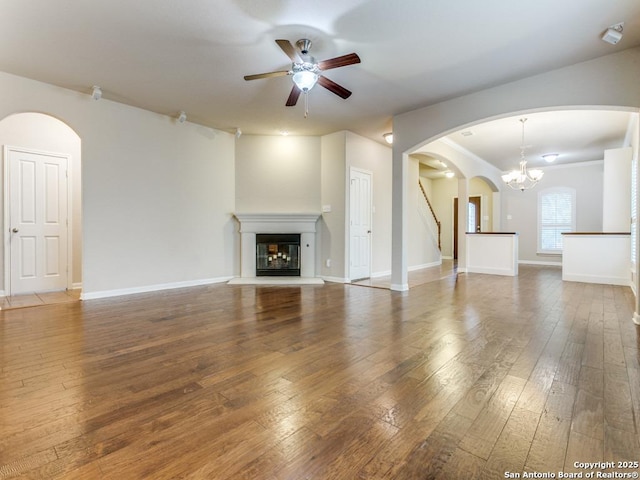 unfurnished living room featuring hardwood / wood-style floors, a ceiling fan, baseboards, arched walkways, and a glass covered fireplace