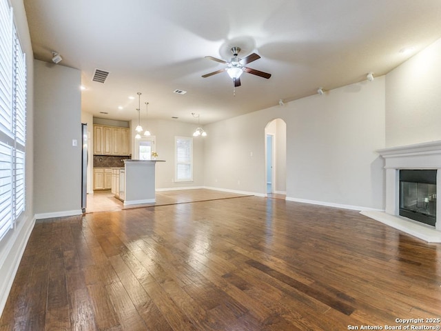 unfurnished living room featuring visible vents, hardwood / wood-style floors, arched walkways, baseboards, and ceiling fan