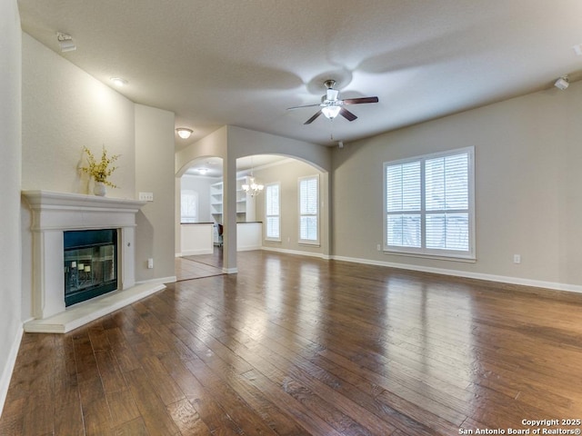 unfurnished living room with hardwood / wood-style floors, ceiling fan with notable chandelier, arched walkways, and a healthy amount of sunlight