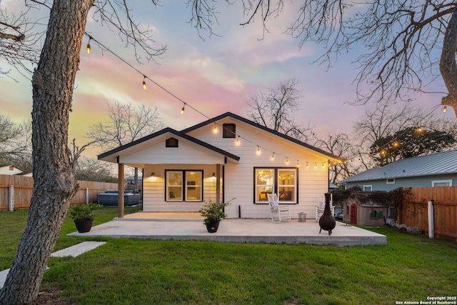 back of property at dusk with a fenced backyard, a lawn, and a patio