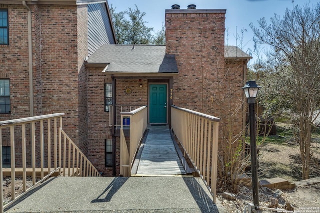 doorway to property with brick siding, a chimney, and roof with shingles