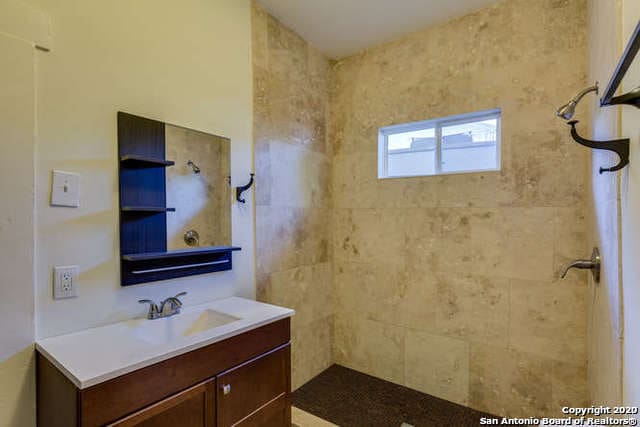 full bathroom featuring a tile shower and vanity