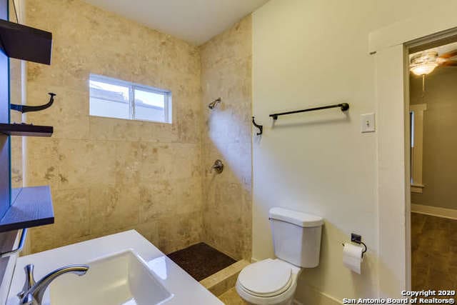 bathroom featuring a sink, toilet, baseboards, and tiled shower