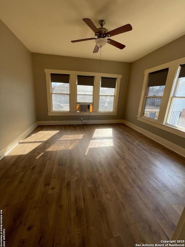 empty room with a healthy amount of sunlight, baseboards, dark wood-type flooring, and ceiling fan