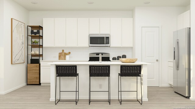 kitchen featuring stainless steel microwave, a breakfast bar, refrigerator with ice dispenser, decorative backsplash, and white cabinetry