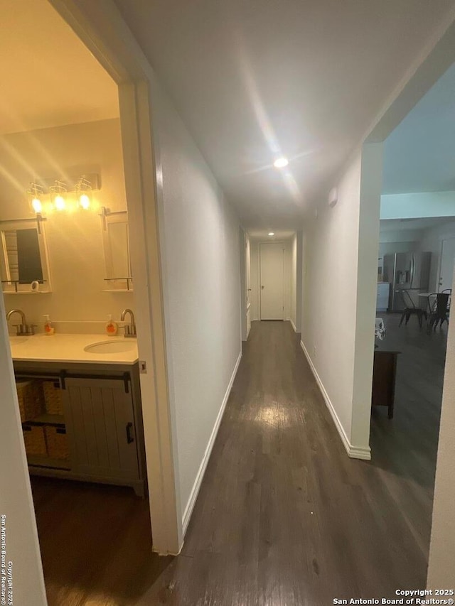 hallway featuring dark wood-style flooring, baseboards, and a sink