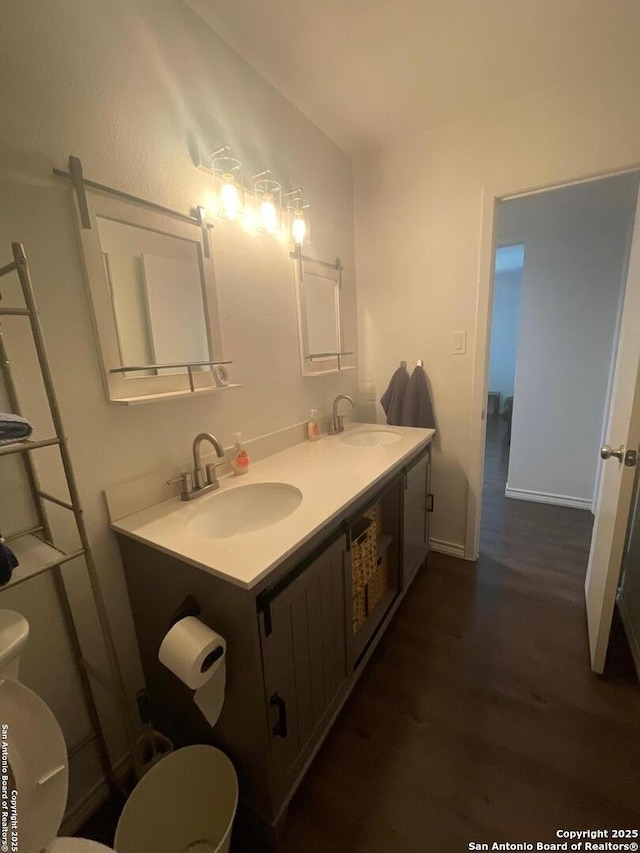 bathroom with double vanity, toilet, wood finished floors, and a sink