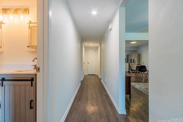 corridor featuring dark wood finished floors, baseboards, and a sink