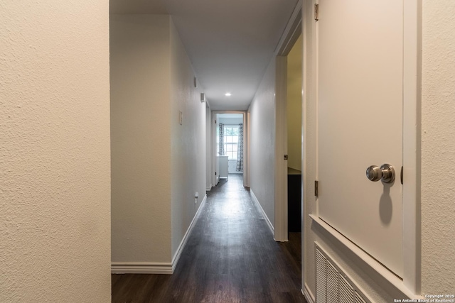 hallway with dark wood finished floors, baseboards, and a textured wall