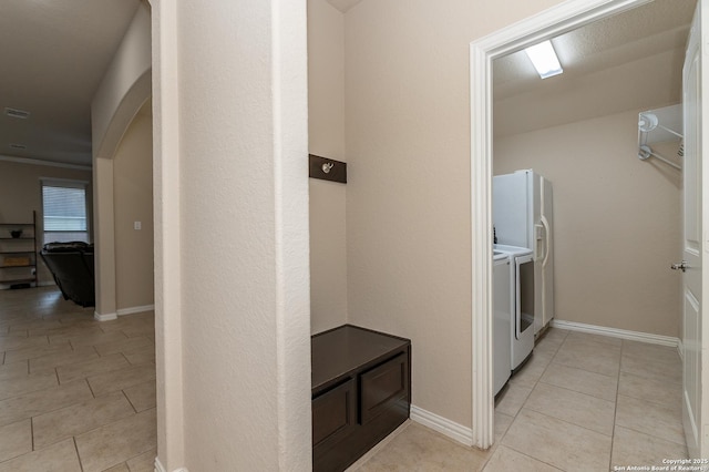 clothes washing area featuring washer and dryer, arched walkways, light tile patterned flooring, baseboards, and laundry area