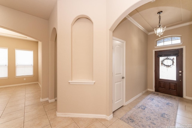 entryway with light tile patterned floors, baseboards, an inviting chandelier, arched walkways, and crown molding