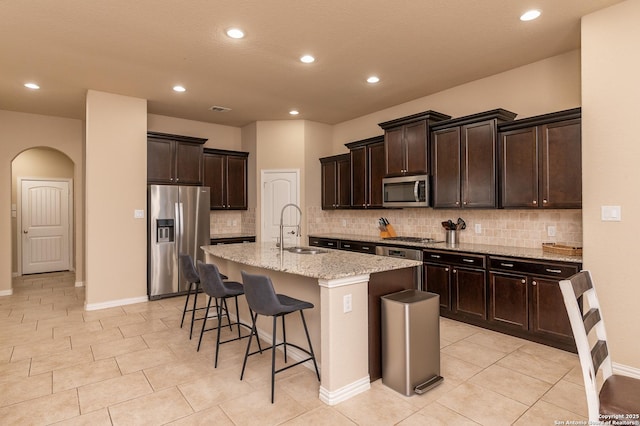 kitchen with light stone countertops, a breakfast bar, arched walkways, a sink, and stainless steel appliances