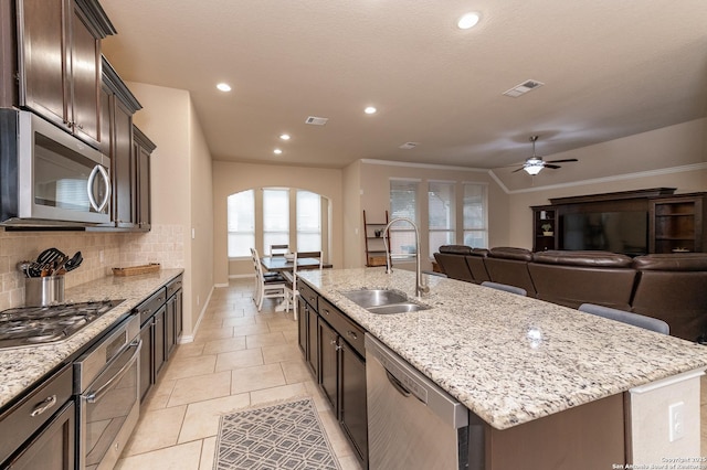 kitchen with a kitchen island with sink, a sink, arched walkways, appliances with stainless steel finishes, and decorative backsplash