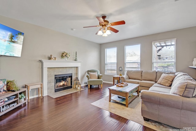 living room featuring baseboards, wood finished floors, a ceiling fan, and a tiled fireplace