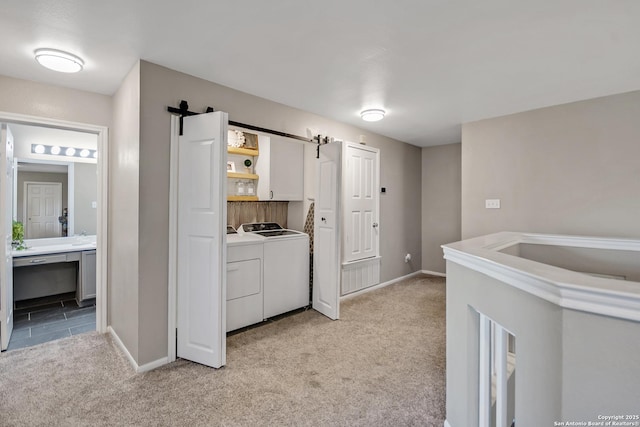 clothes washing area with washing machine and clothes dryer, baseboards, light colored carpet, a barn door, and laundry area