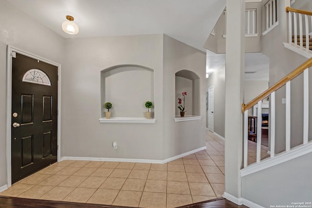 foyer entrance featuring stairs, light tile patterned flooring, and baseboards