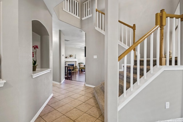 foyer with stairway, arched walkways, a high ceiling, light tile patterned floors, and baseboards